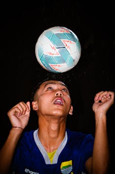 An intense action shot of a young soccer player heading the ball under bright stadium lights.
