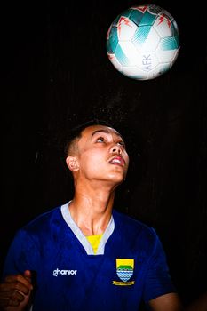Focused young athlete practices soccer heading with precision under spotlight.