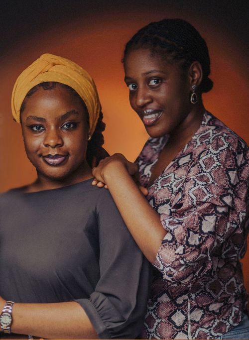 Free Elegant portrait of two women with a warm, rich background and stylish attire. Stock Photo