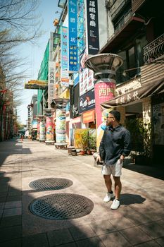 A fashionable man walks down a vibrant street in Taipei, Taiwan. Urban exploration vibe.