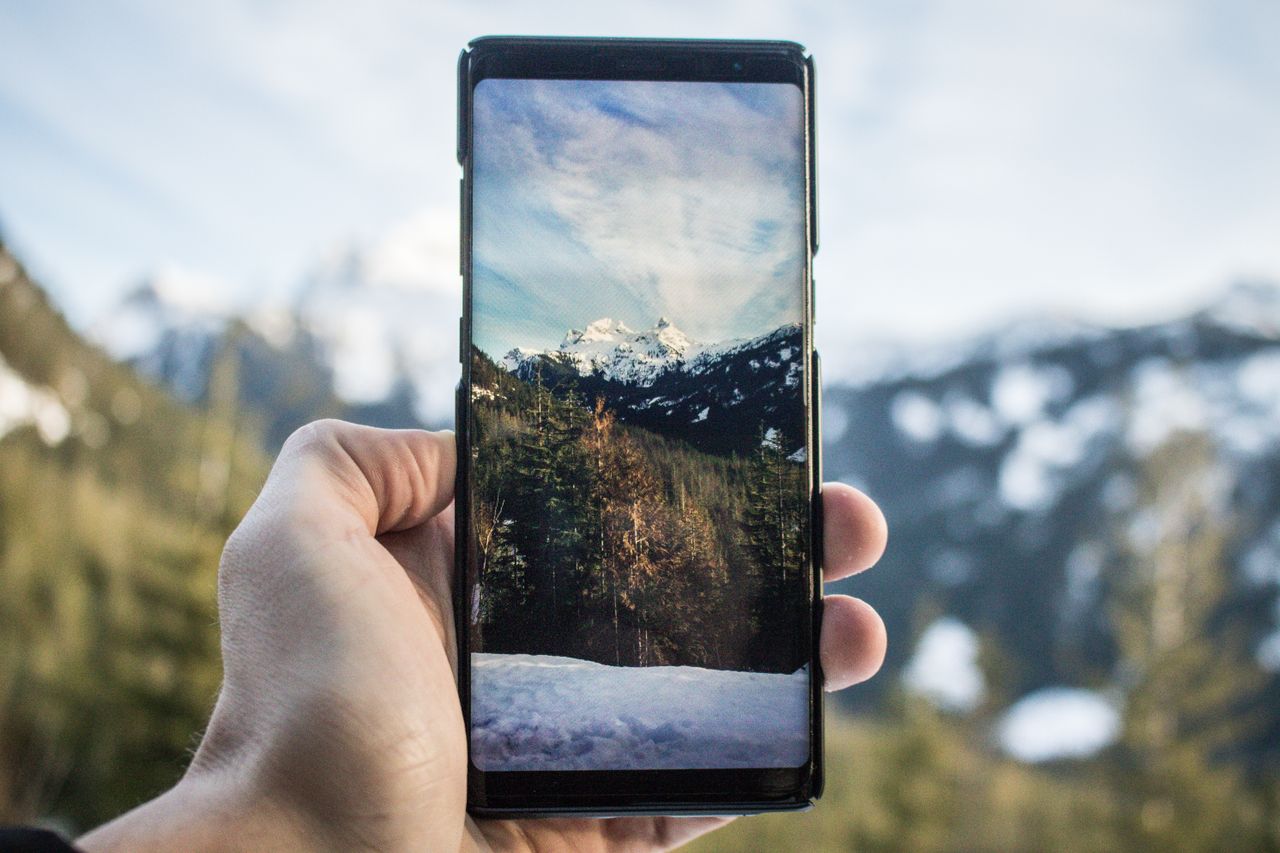hand holding a smartphone displaying a mountain view snowy peaks and f