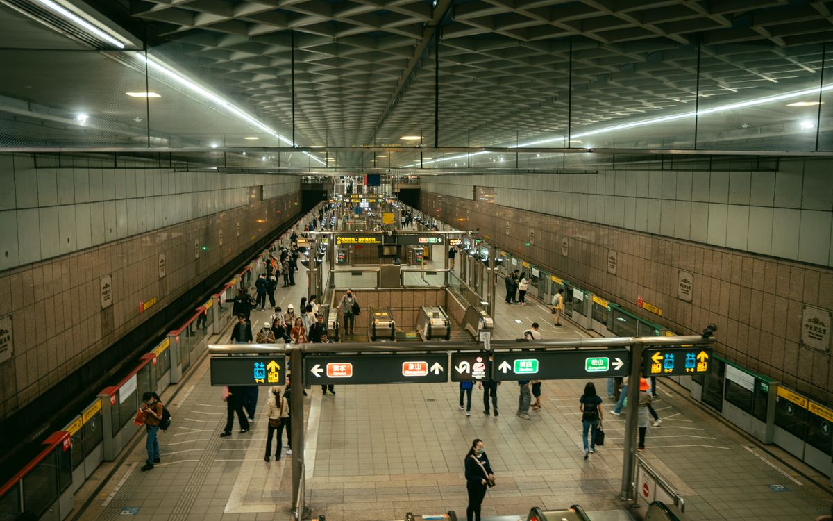 A busy Taipei Metro station with commuters navigating escalators and platforms during rush hour.