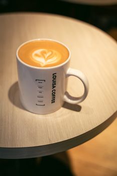 A beautifully crafted latte with heart-shaped art in a Louisa Coffee mug on a wooden table.