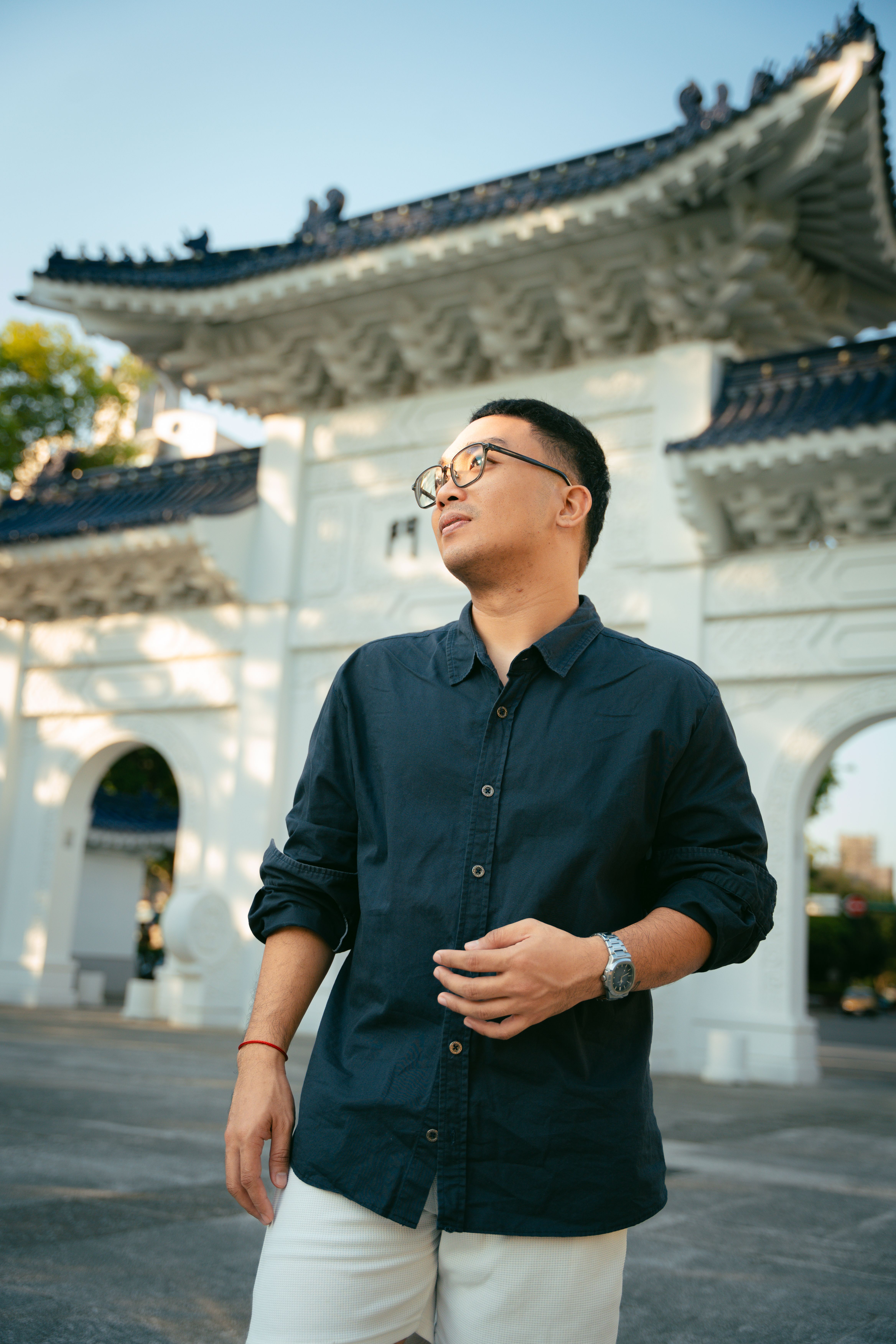 Young man in casual attire posing in front of a traditional Chinese architectural gateway.