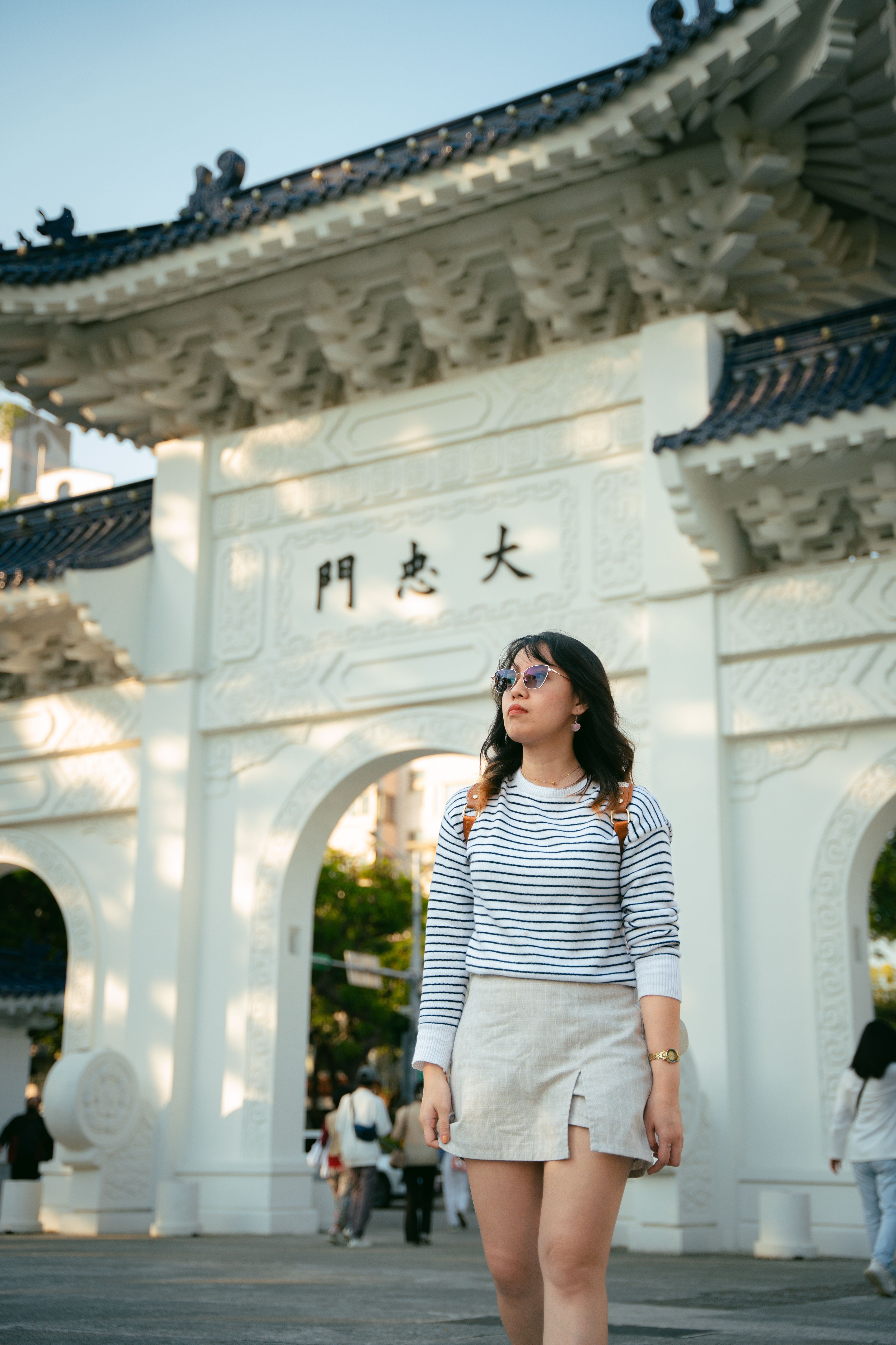 Woman in striped outfit standing outside the gate at Liberty Square, showcasing urban fashion.