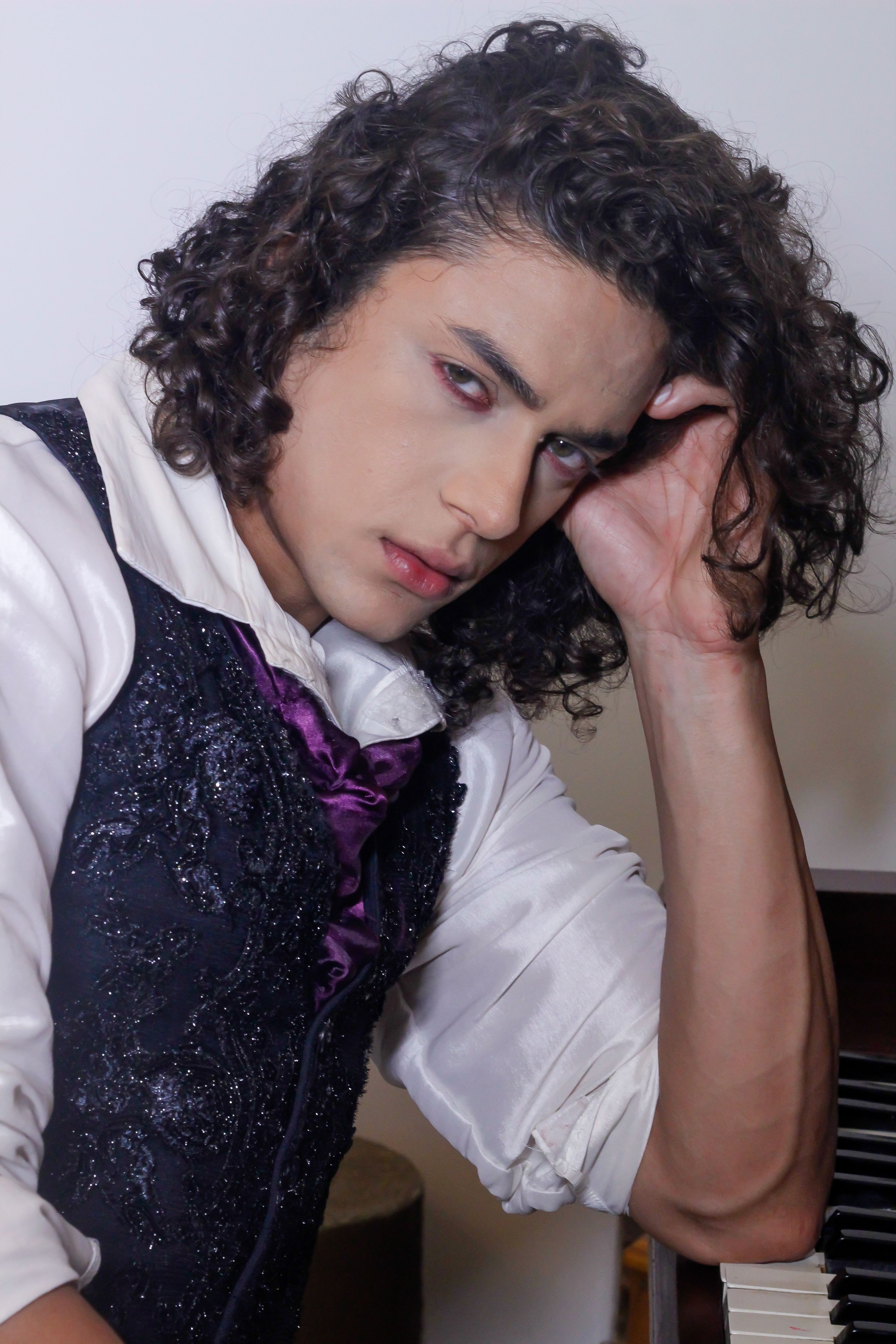 Sophisticated portrait of a man in vintage attire posing by a piano indoors.