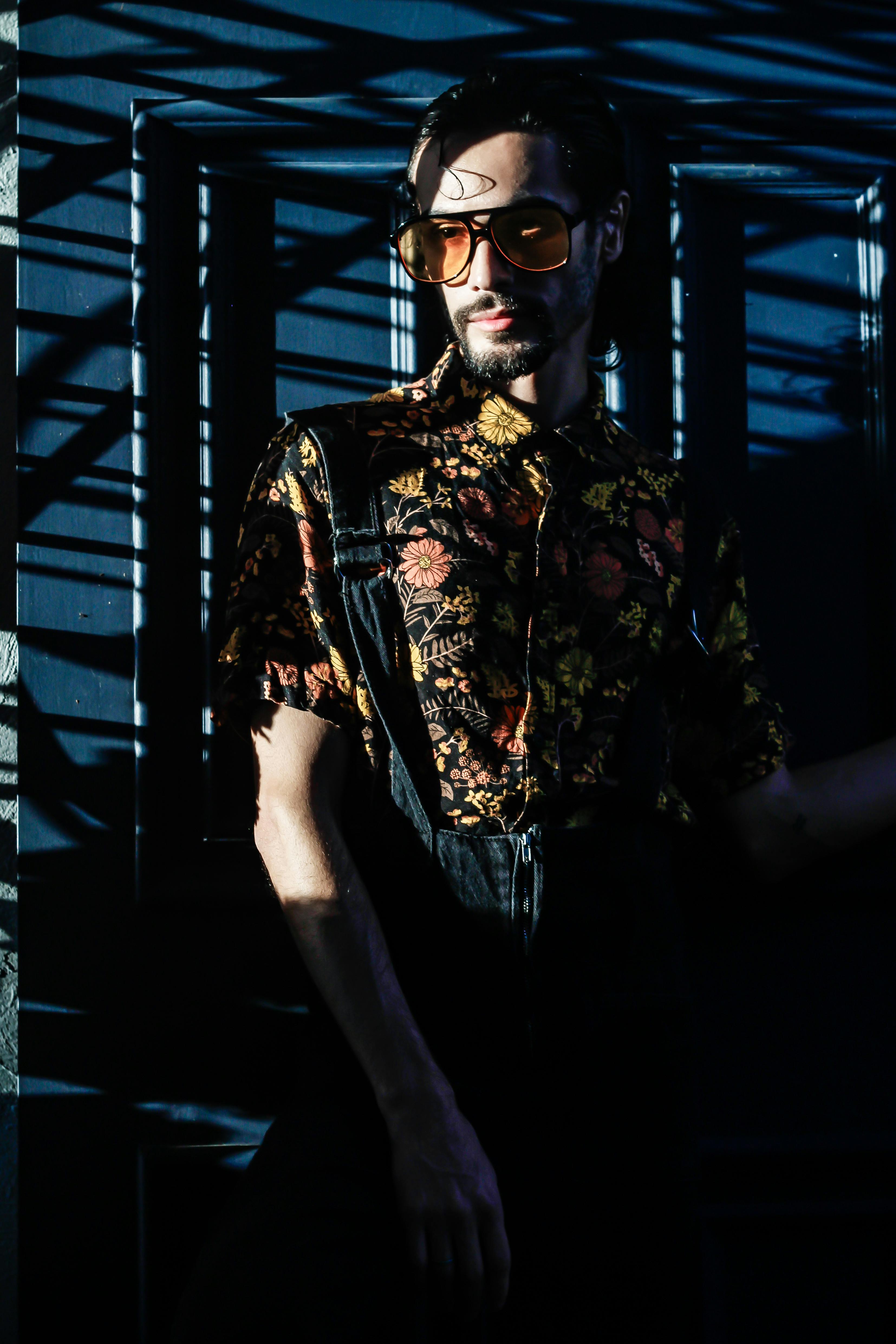 Stylish man wearing floral shirt and sunglasses in dramatic shadow lighting.