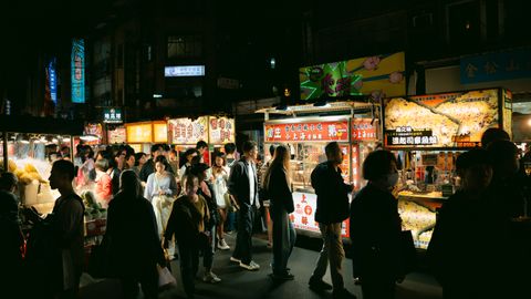 Crowded night market with food stalls offering a variety of dishes and a lively atmosphere.