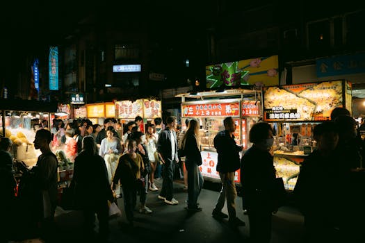 Crowded night market with food stalls offering a variety of dishes and a lively atmosphere.