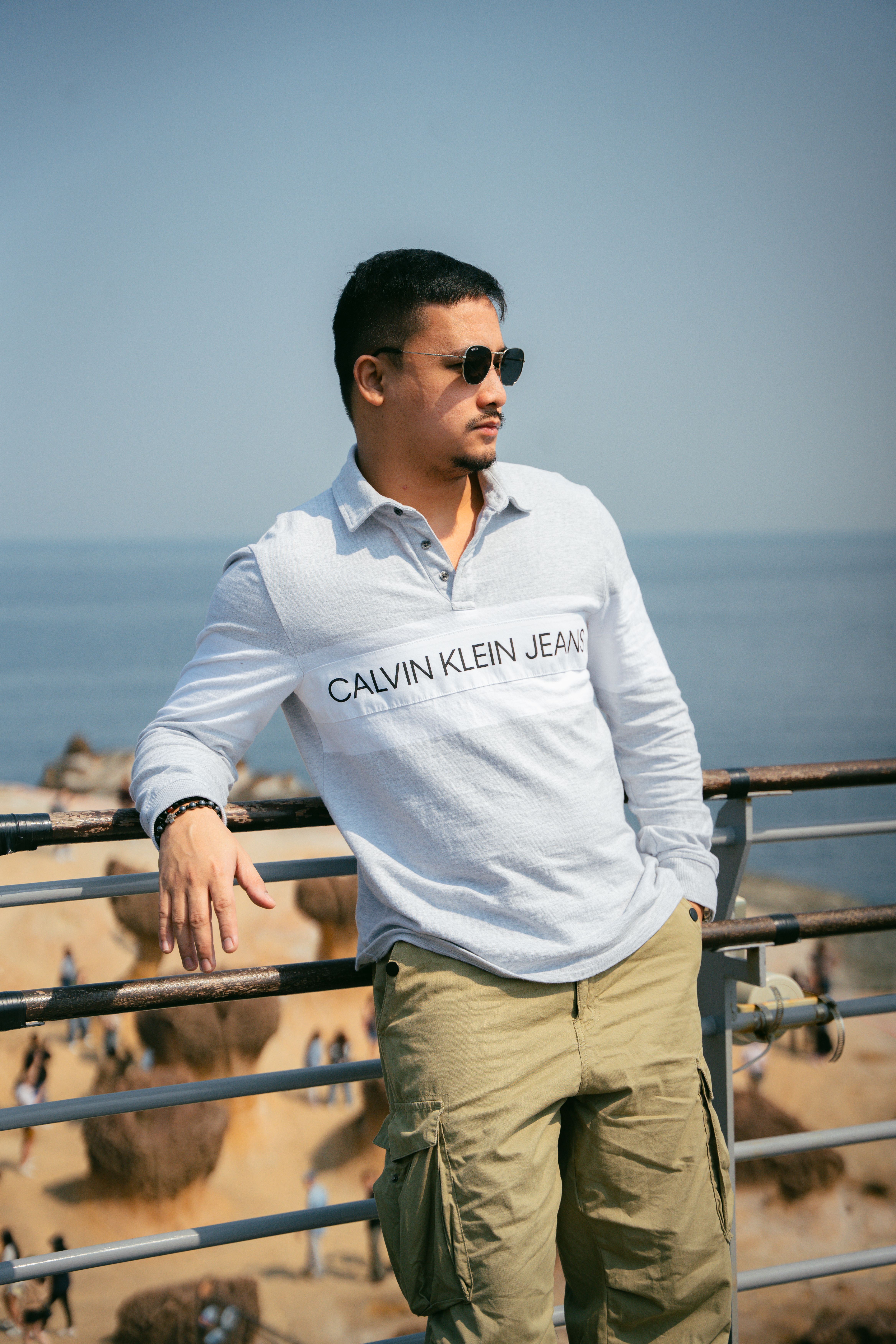 Casual man leaning on balcony overlooking the sea on a sunny day.