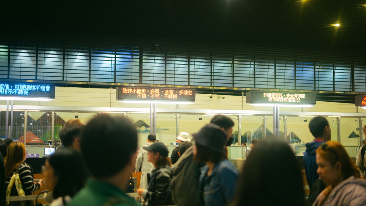Crowded airport check-in area with people queueing and visible flight information signs.