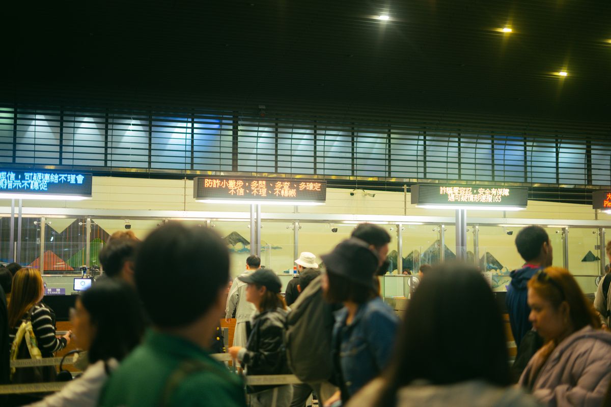 A crowded airport check-in area with travellers queuing and luggage trolleys