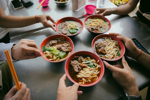 Top view of people sharing delicious beef noodle soup with chopsticks. Vibrant and inviting meal setting.