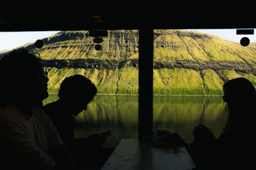 Silhouettes of people in a cafe with stunning lake and mountain views, capturing serene nature and travel vibes.