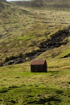 A lonely rustic cabin situated in a lush, green mountain valley under a clear sky.