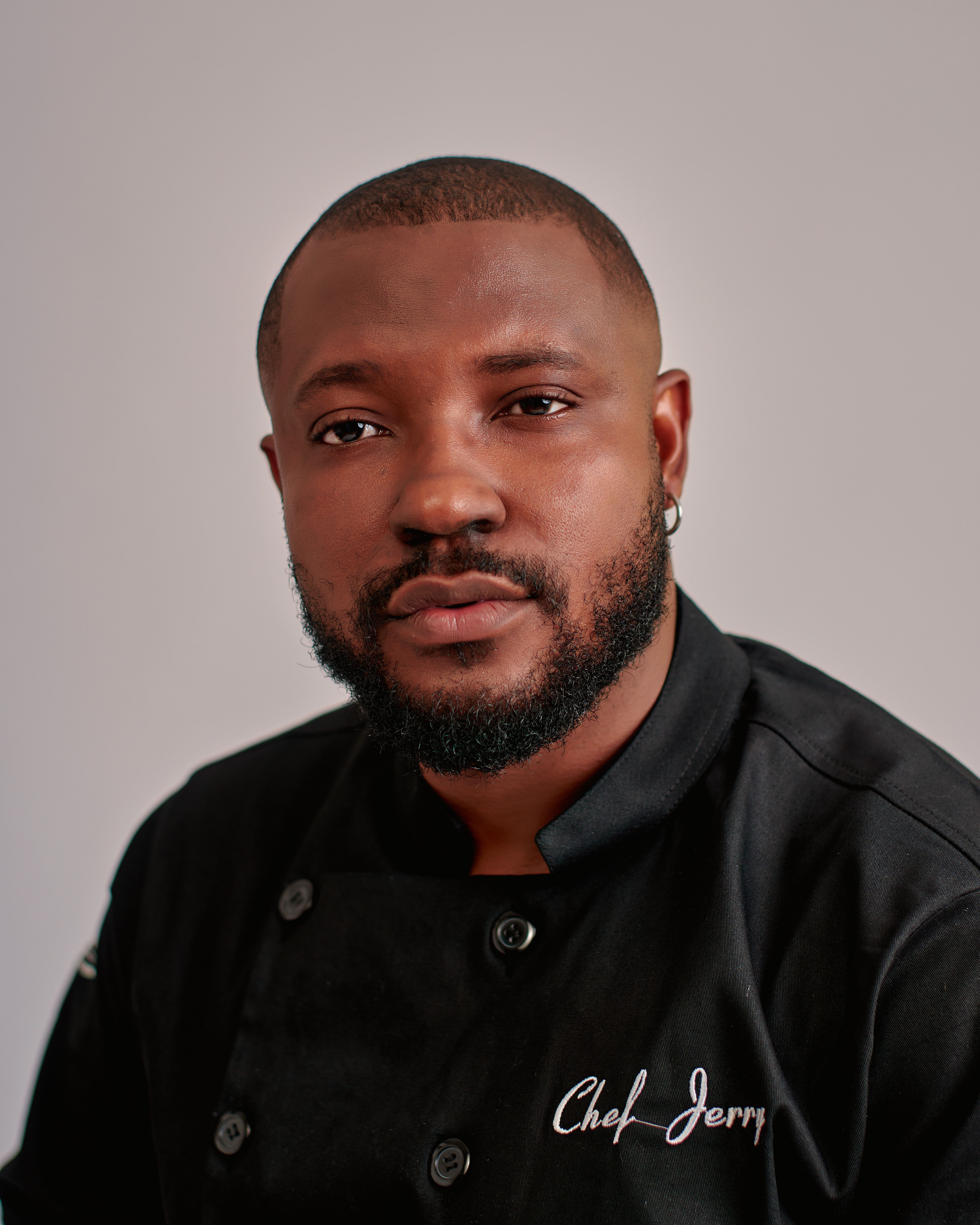 Portrait of a professional chef wearing a black uniform with a neutral background.