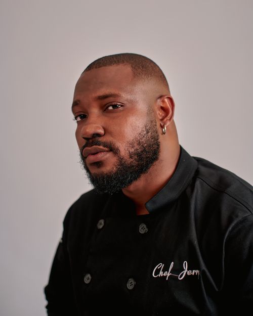 Free Professional chef posing confidently in a black uniform against a neutral backdrop. Stock Photo