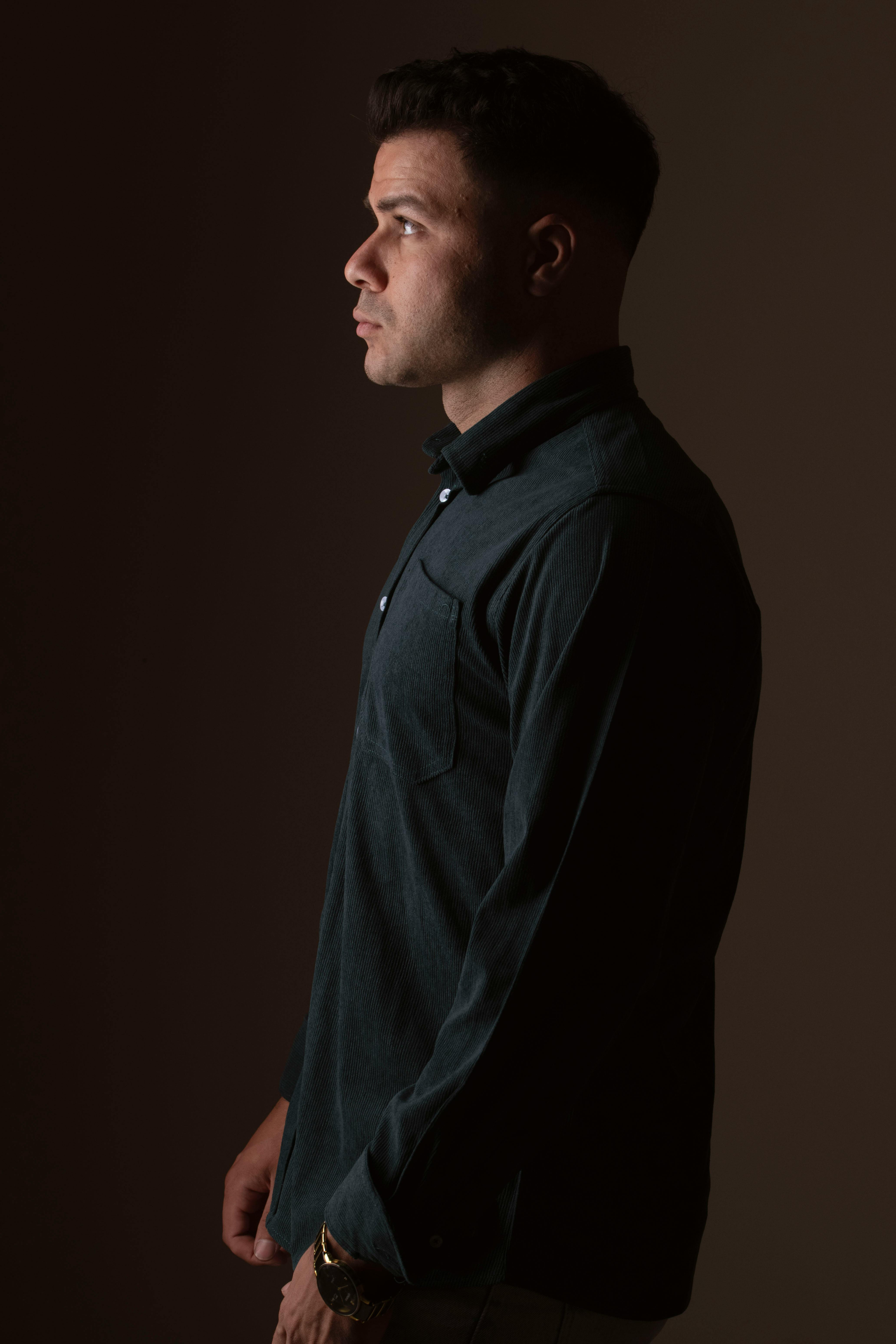 A thoughtful side profile of a man in a dark shirt against a muted background.