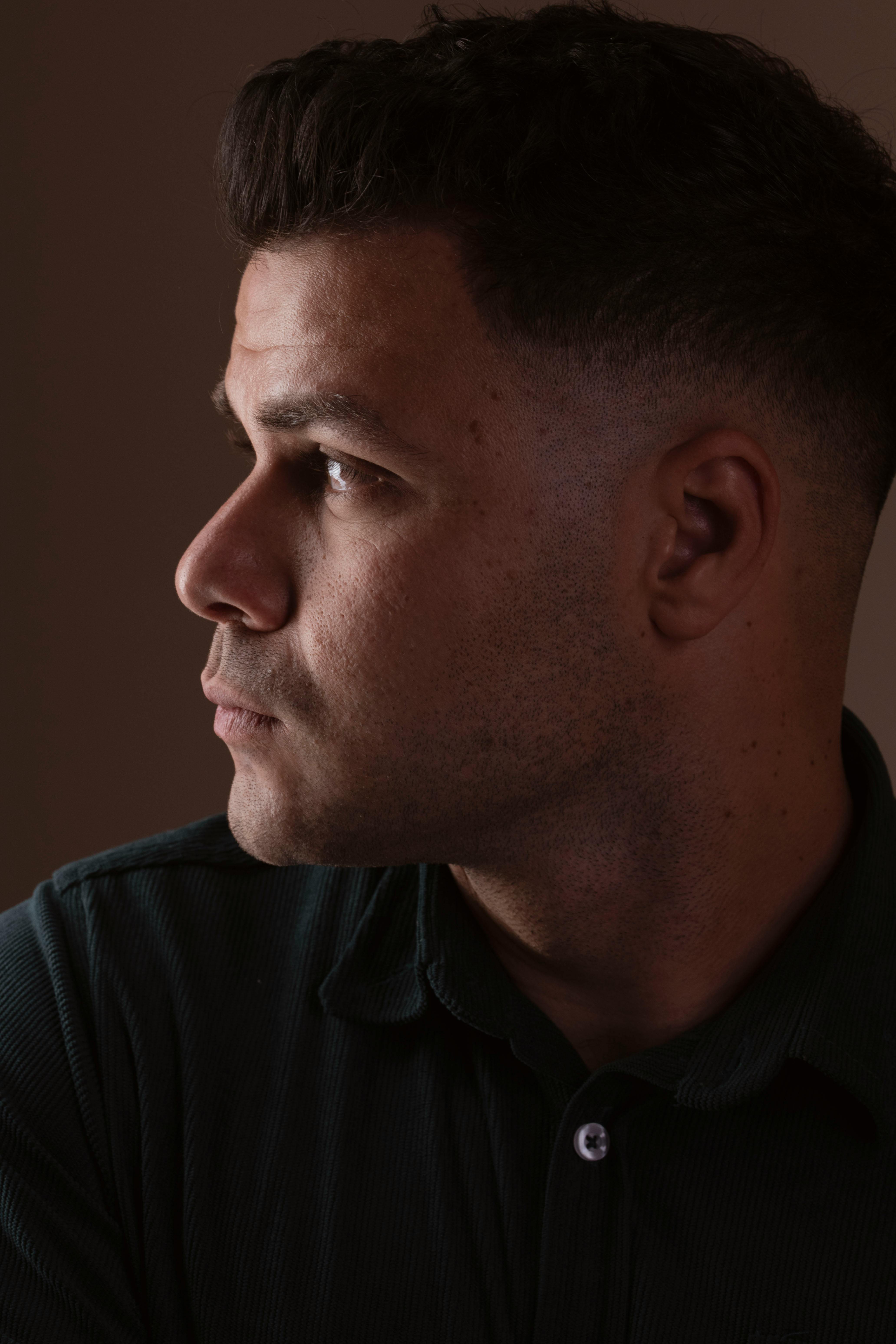 Moody portrait of a man looking to the side, creating a thoughtful ambiance in soft lighting.