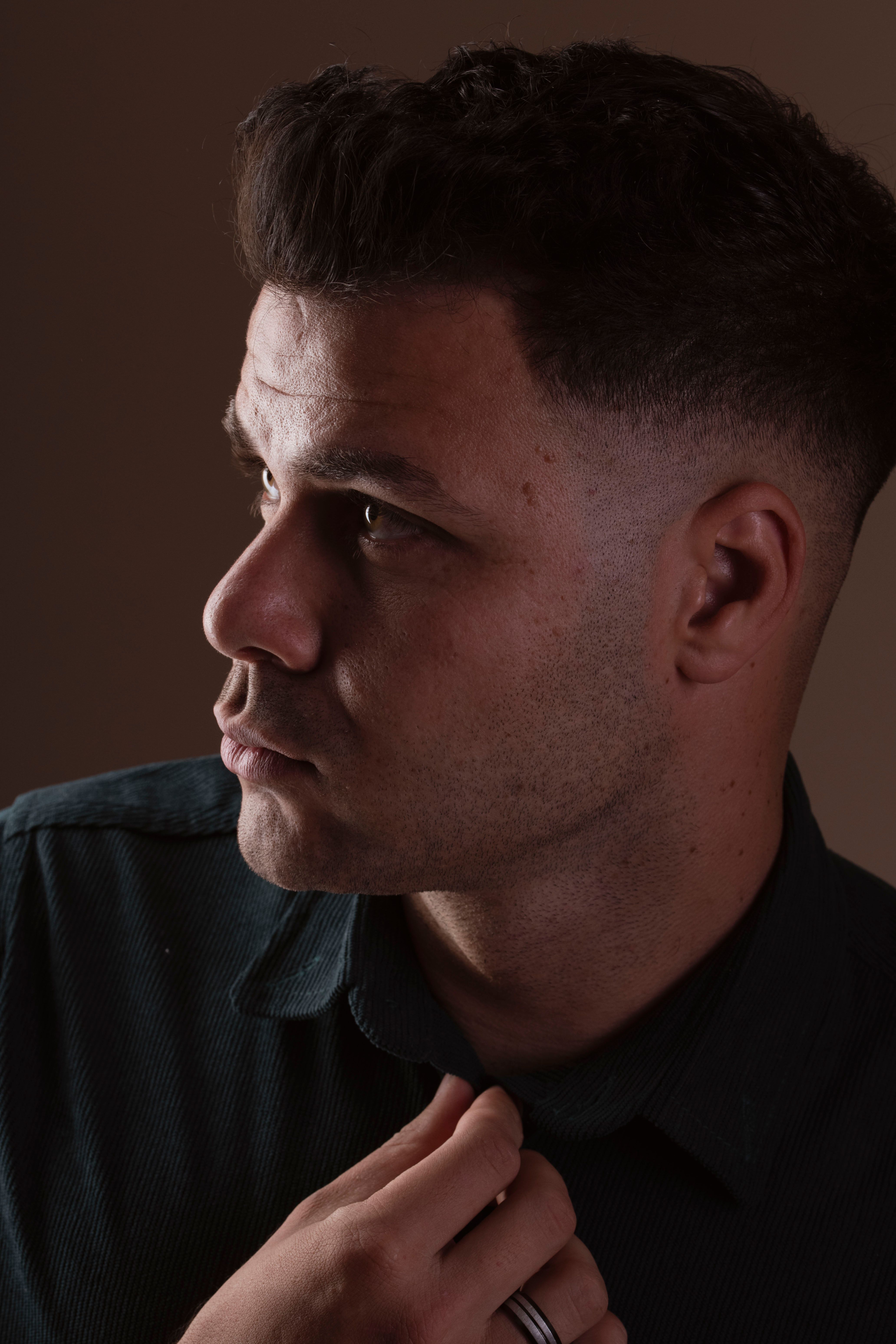 Introspectief zijprofielportret van een jonge man tegen een donkere achtergrond