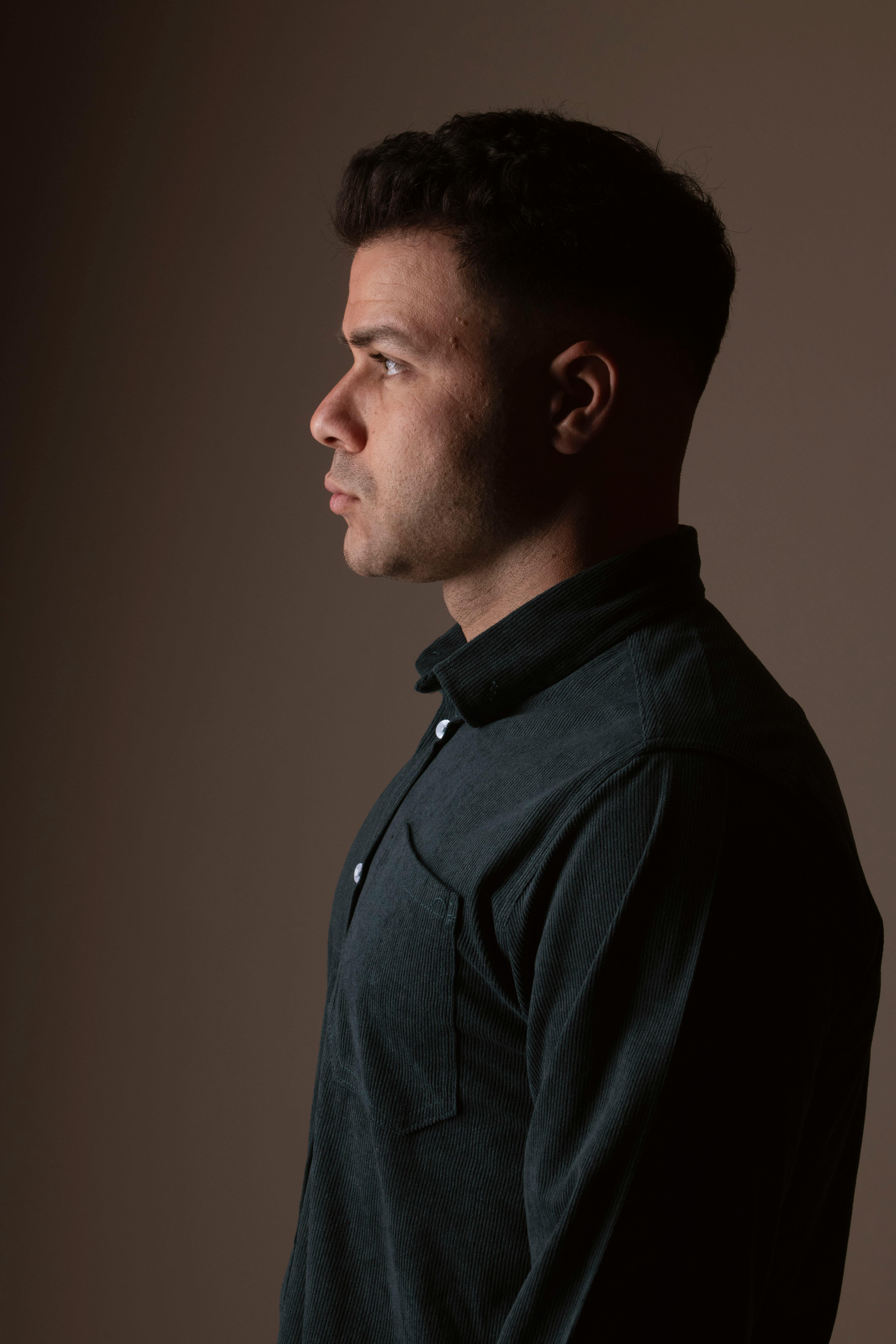 A side profile portrait of a man in a dark shirt looking left against a plain background.