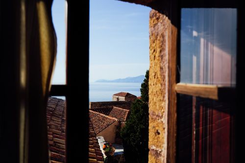 Free Charming Mediterranean coastal view through a rustic window with terracotta rooftops and sea horizon. Stock Photo