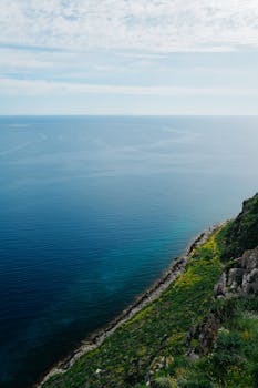 Breathtaking view of a steep, green cliff meeting the vast blue ocean beneath a cloudy sky.