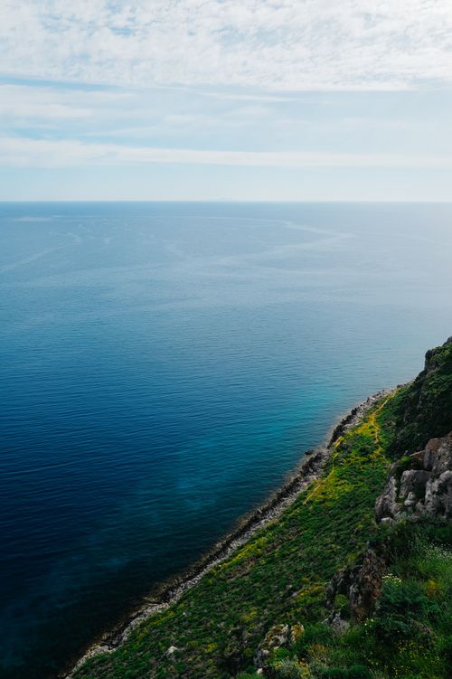 Free Breathtaking view of a steep, green cliff meeting the vast blue ocean beneath a cloudy sky. Stock Photo