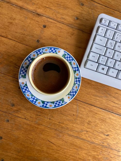 Free Top view of coffee in floral cup beside keyboard on wooden surface. Stock Photo