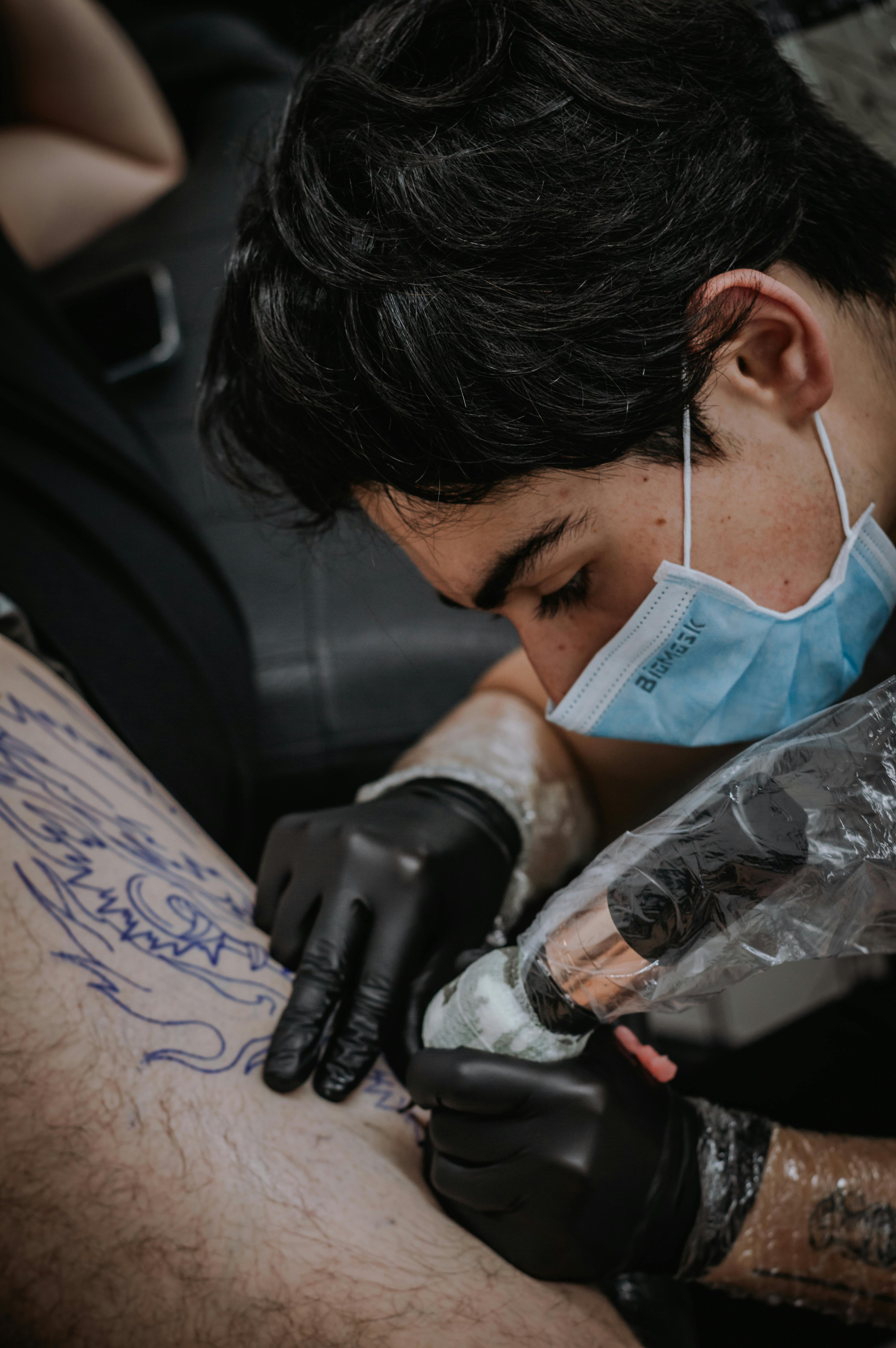 A focused tattoo artist works meticulously on a client's intricate leg design in a Bogotá studio.