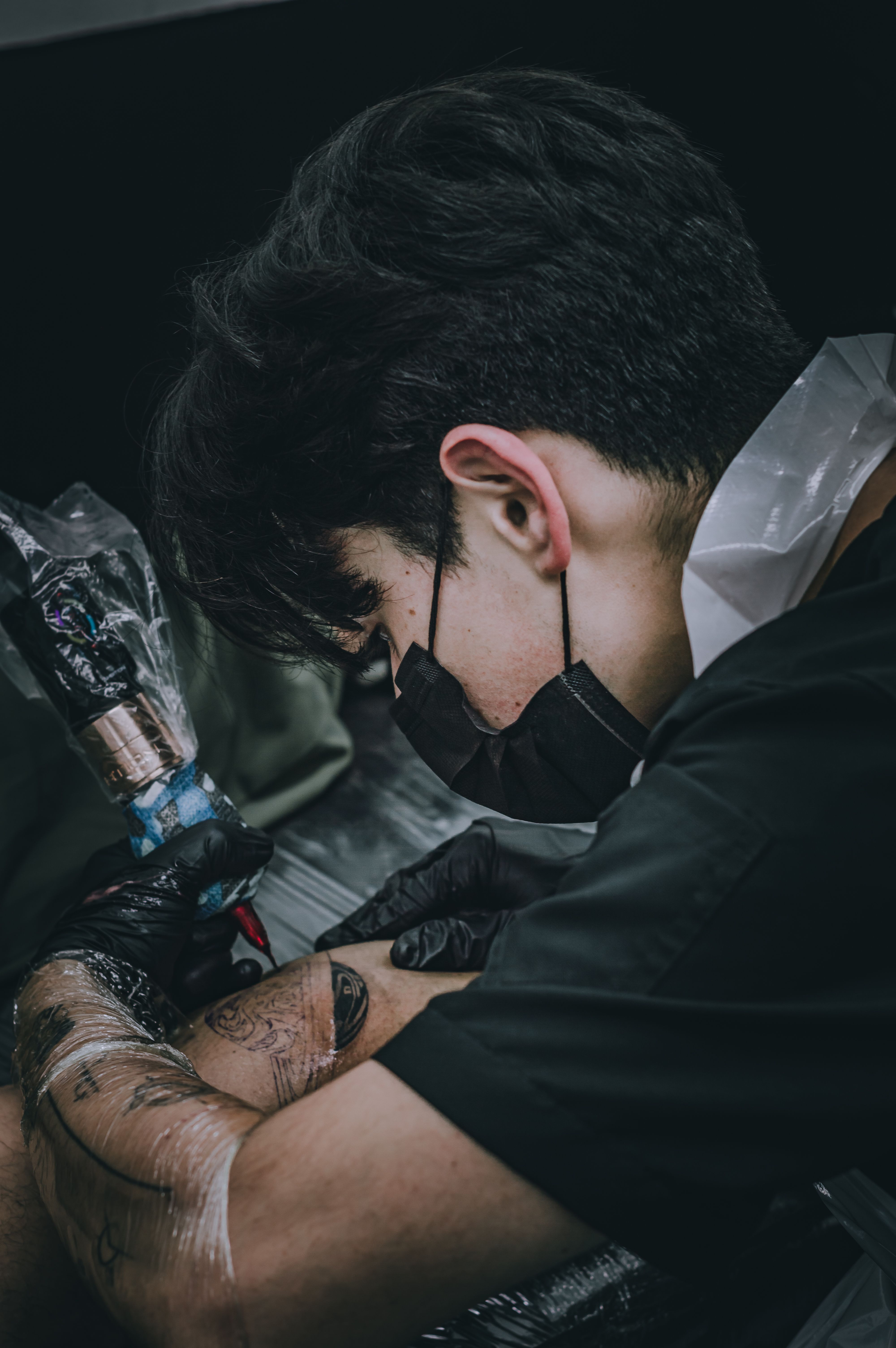 Tattoo artist focused on creating a detailed design in a Bogotá studio. Dark and artistic tone.