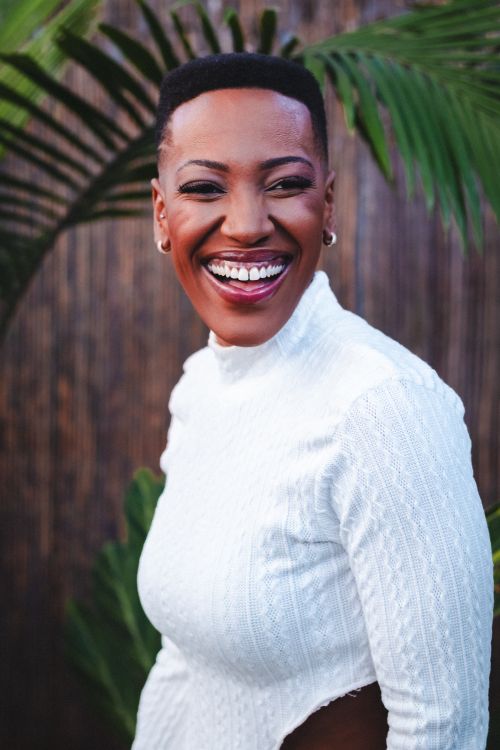Free Portrait of a smiling woman in a white sweater, set against lush greenery in São Paulo. Stock Photo