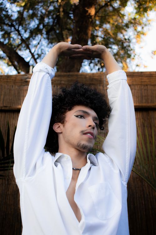 Free Man with curly hair in a white shirt posing under trees outdoors. Stock Photo