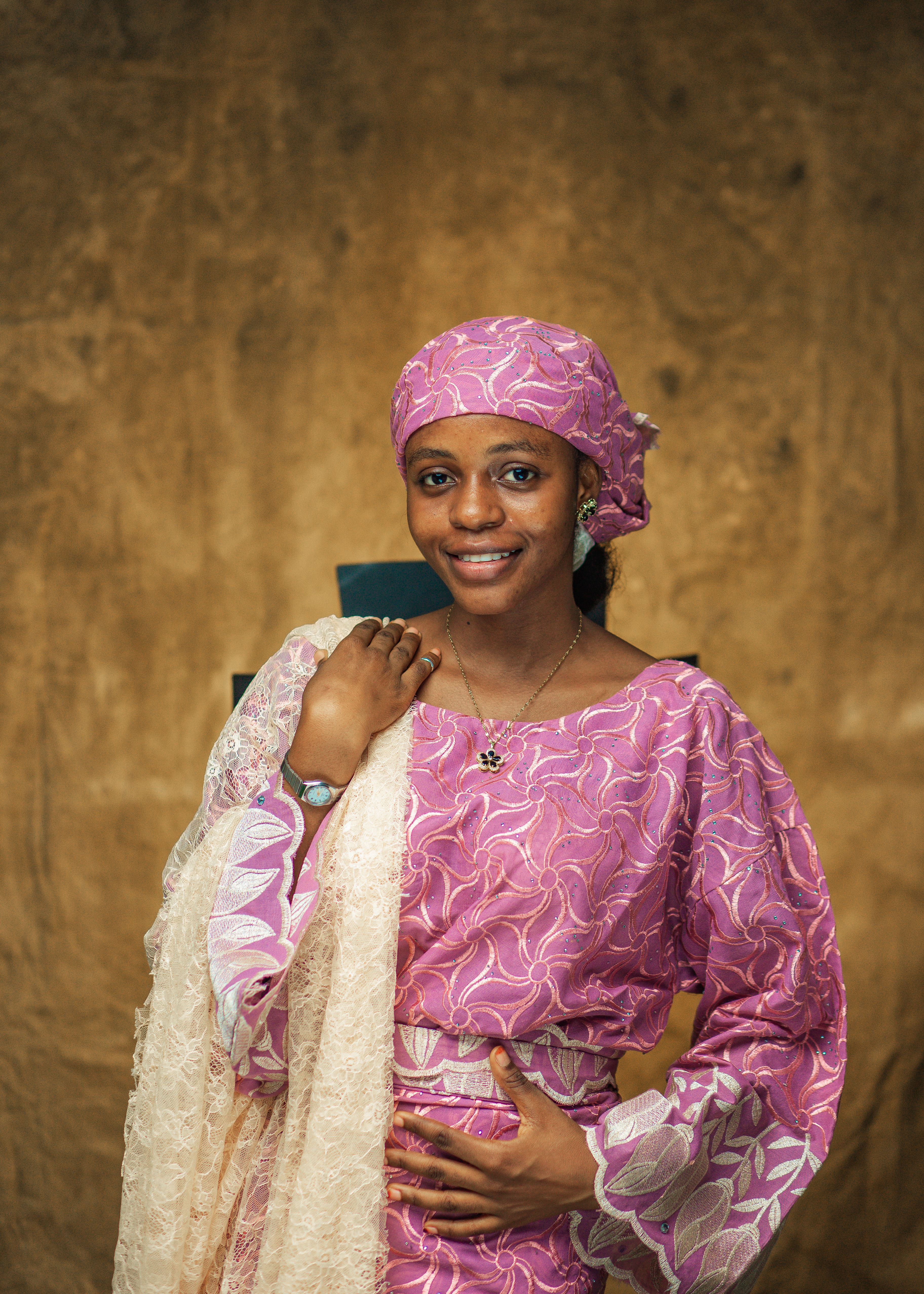 Smiling woman in pink African dress and headscarf poses confidently indoors.