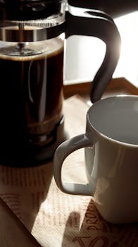 Inviting scene of freshly brewed French press coffee beside an empty white mug.