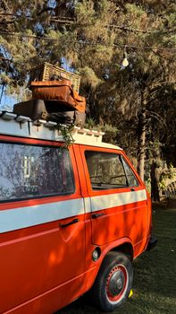 Retro orange van with luggage on top, parked in a serene forest setting.