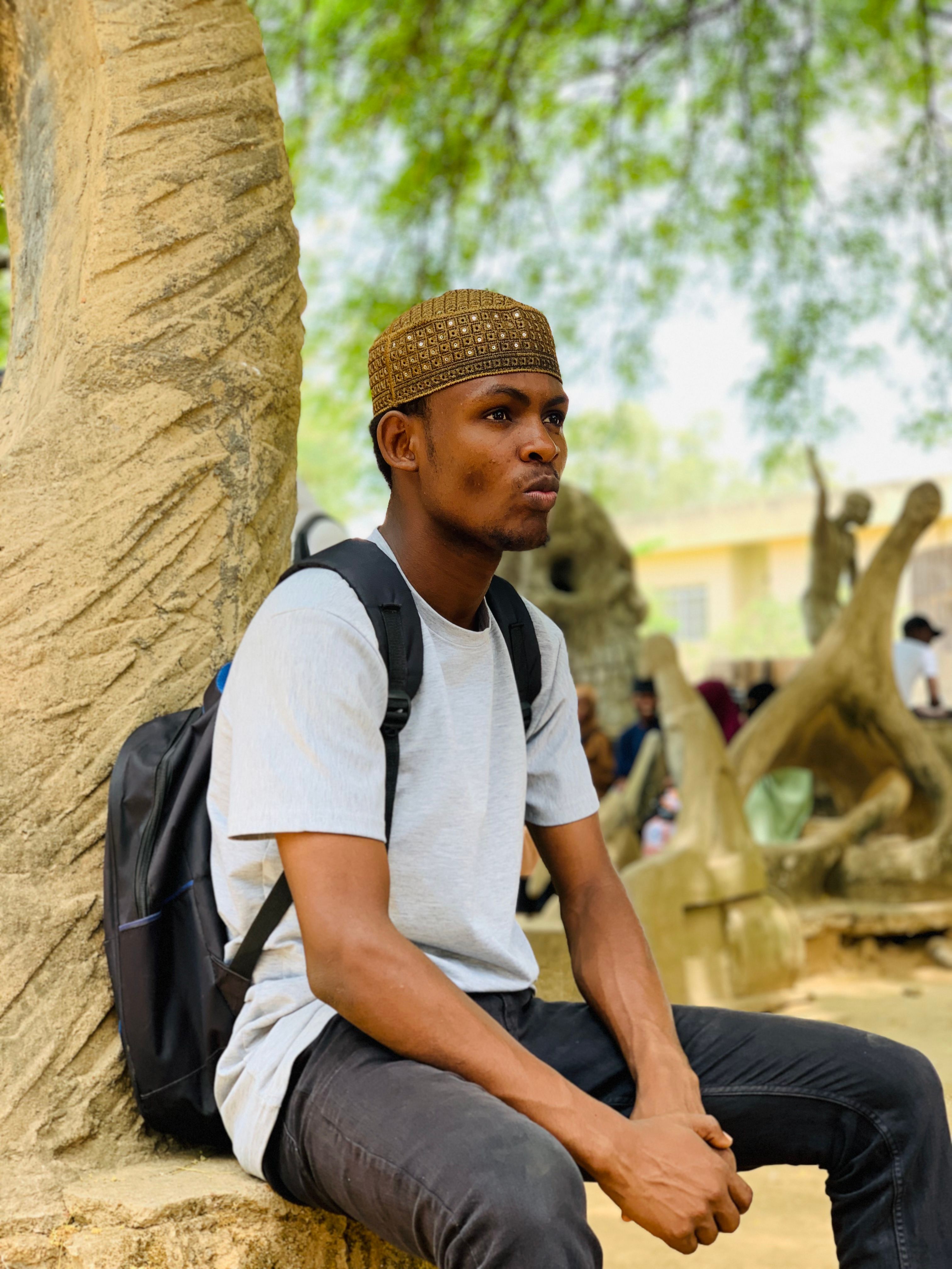 Portrait of a young man sitting outdoors, surrounded by sculpted trees and a sunny, tranquil environment.