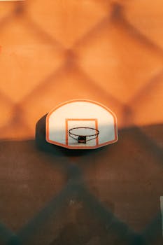 A basketball hoop with shadows at sunset creates a dramatic outdoor sports scene.