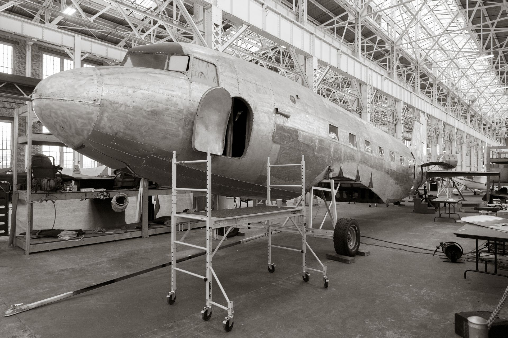 A classic aircraft undergoes restoration inside a spacious hangar, showcasing industrial architecture.