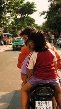 Children ride together on a motorcycle in a vibrant city street.