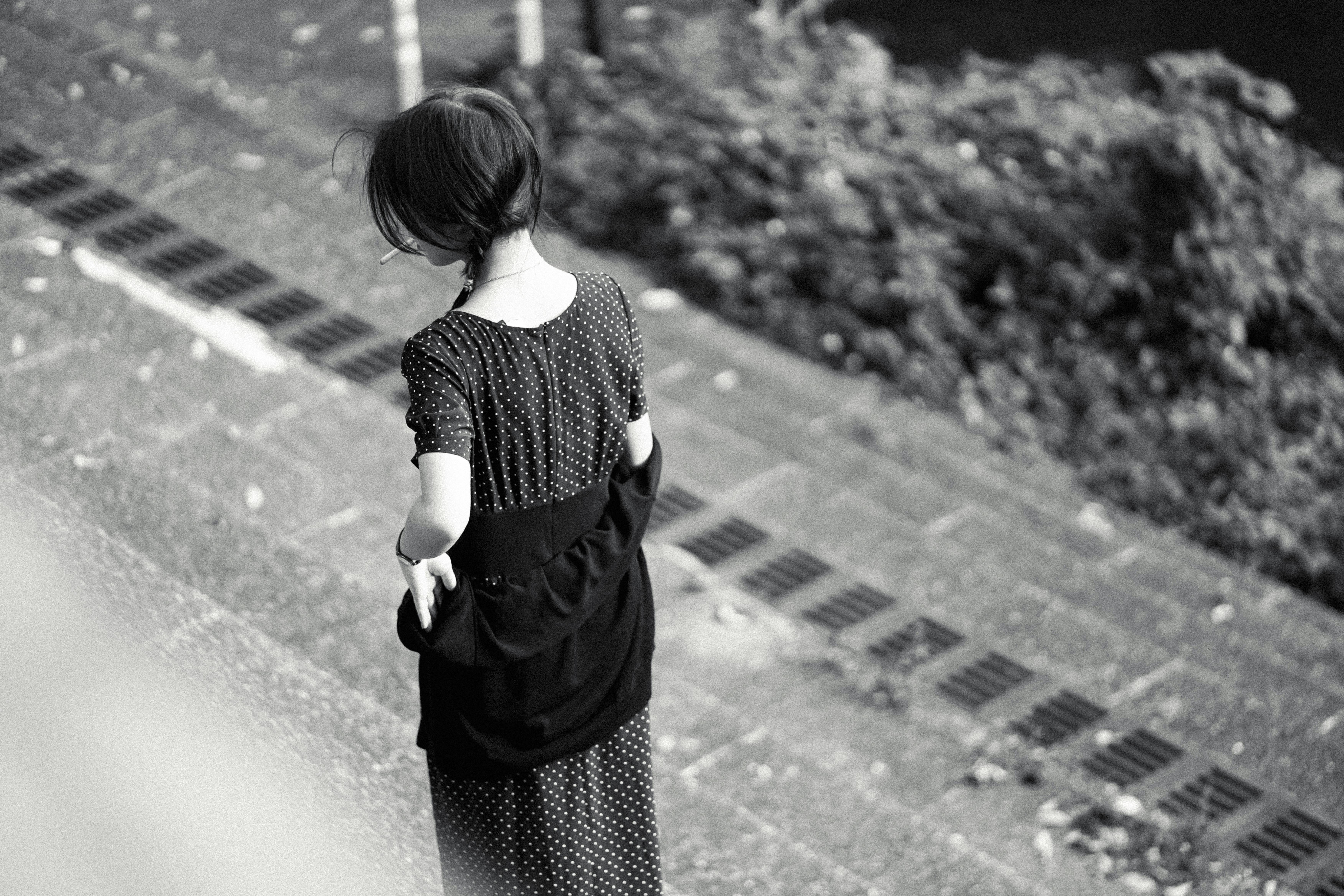 水玉模様のドレスを着た女性が屋外の舗装された小道を歩いている後ろ姿の白黒画像。