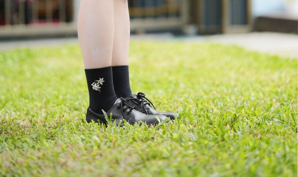 A pair of black shoes with floral socks stands on a vibrant green lawn. Perfect for outdoor, fashion, and lifestyle themes.