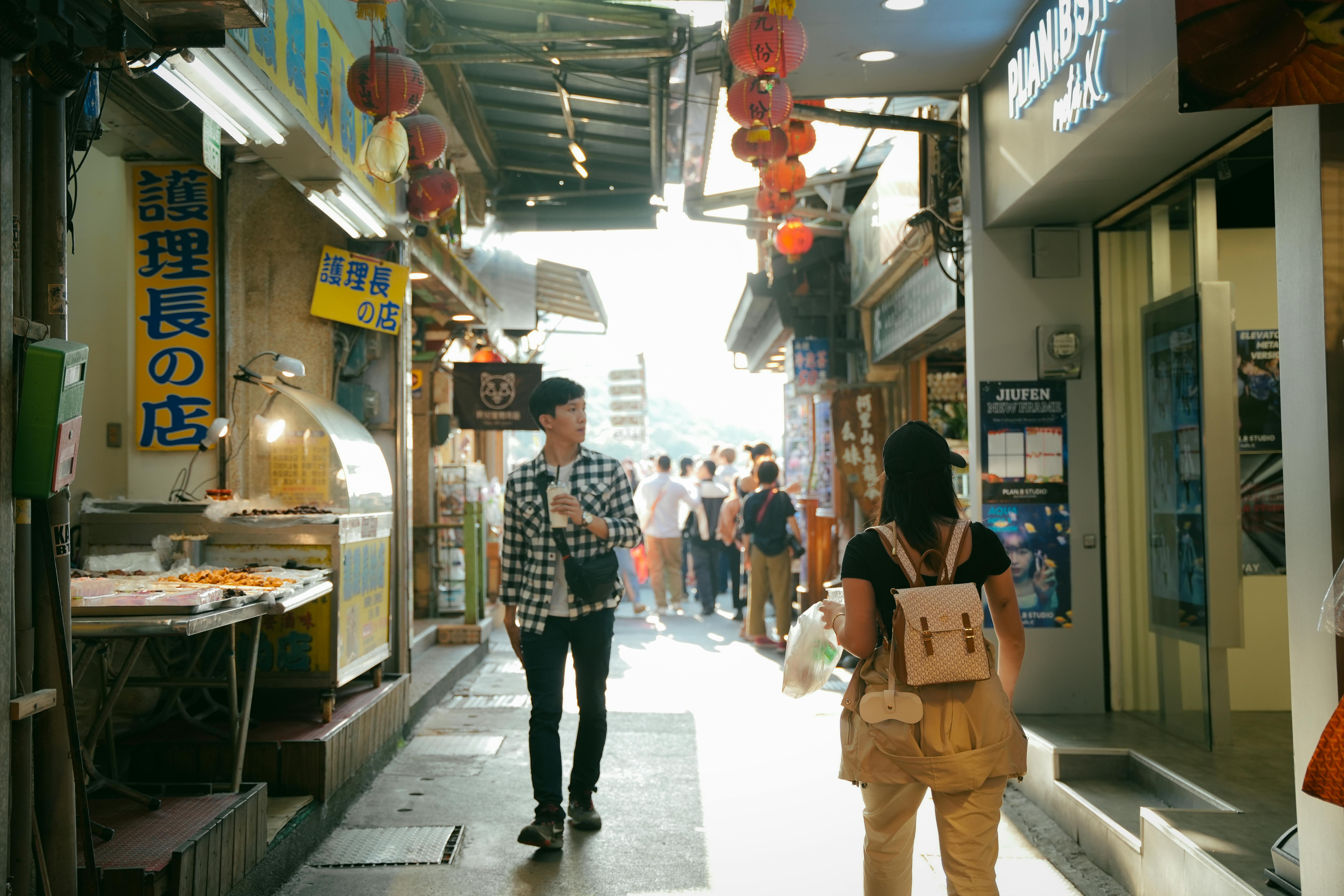 Shoppers exploring vibrant Jiufen street market under sunlight with food stalls and lanterns