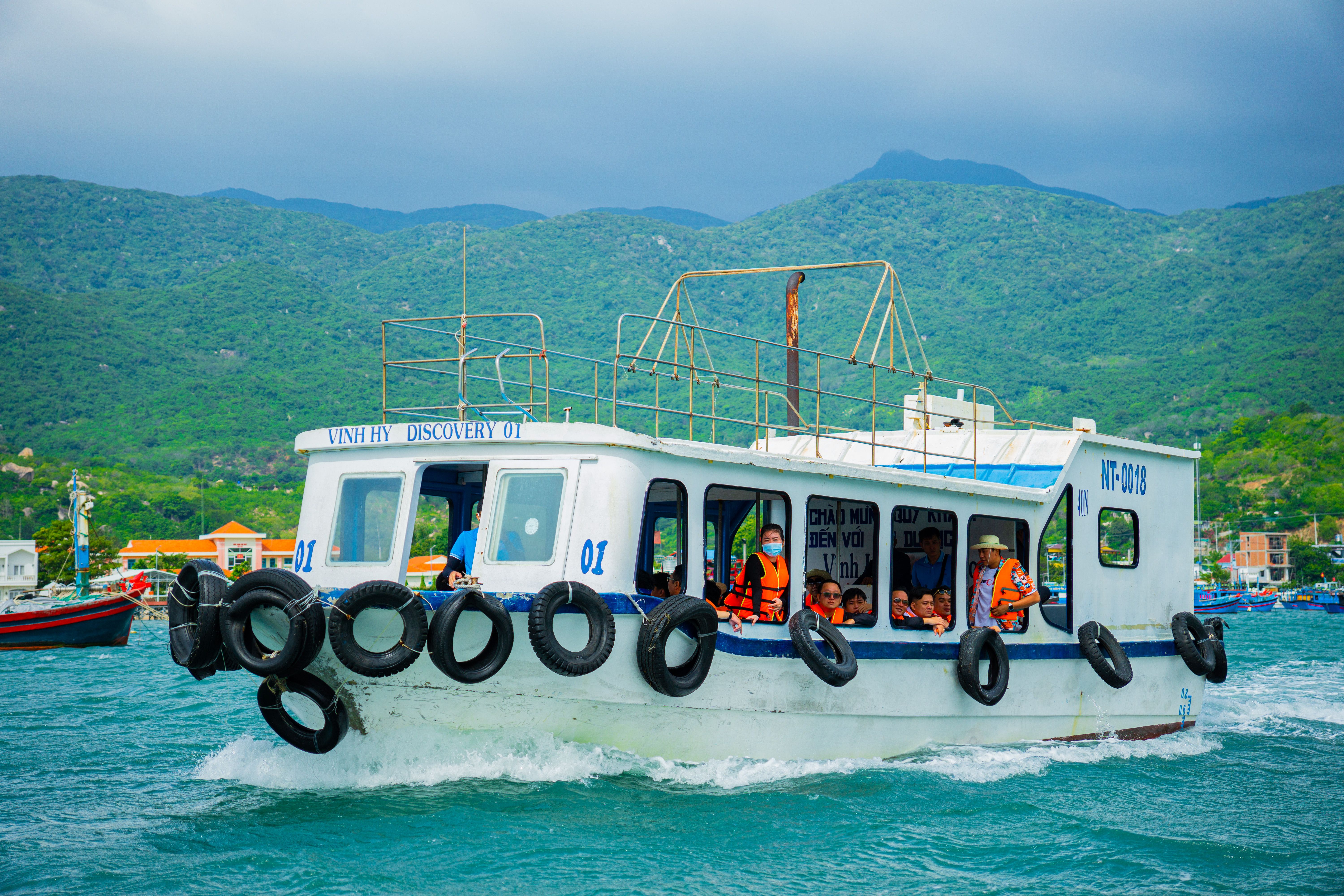 Tourist boat cruising through Vinh Hy Bay with lush green mountains in the background.