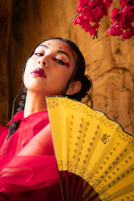 Portrait of a woman in red with a traditional Chinese fan and floral decorations.