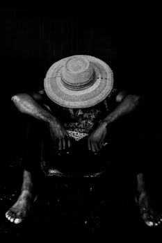 一张戏剧性的黑白照片中，一个人头戴遮阳帽遮住脸庞坐在那里，营造出一种喜怒无常的氛围