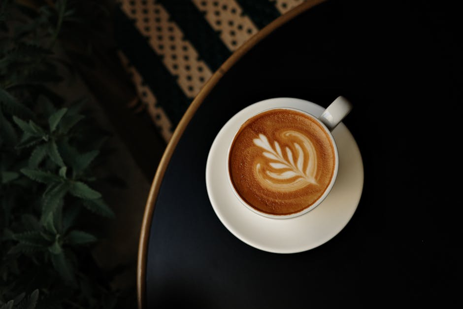 A top-view of a latte with intricate art in a white cup on a dark table, perfect for coffee lovers.