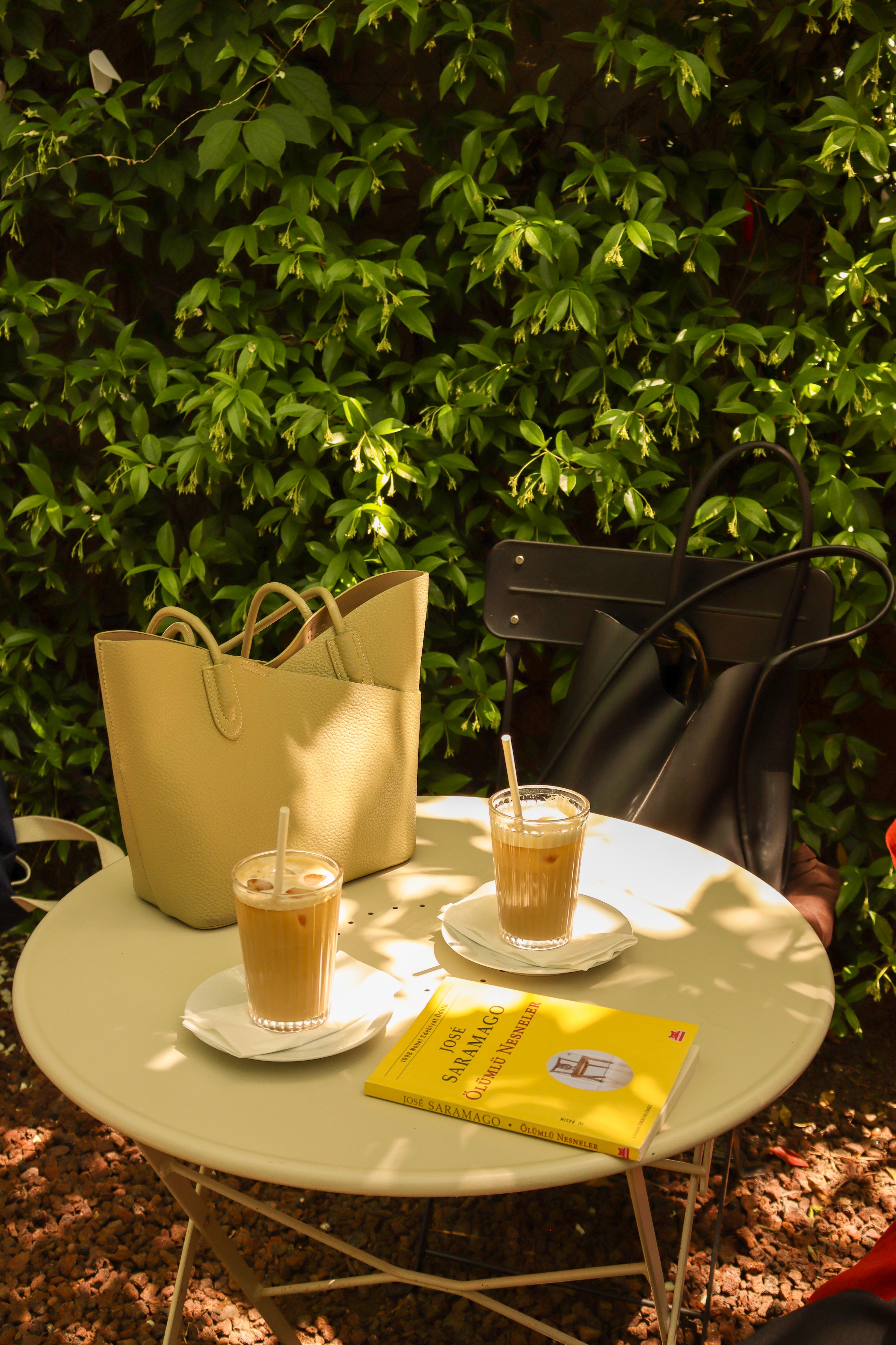 Sunny outdoor cafe table with iced coffee, bags, and a book, creating a relaxed ambiance. - How to Match Handbags with Outfits