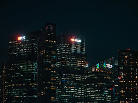Illuminated city skyscrapers of major banks in Singapore's financial district at night.
