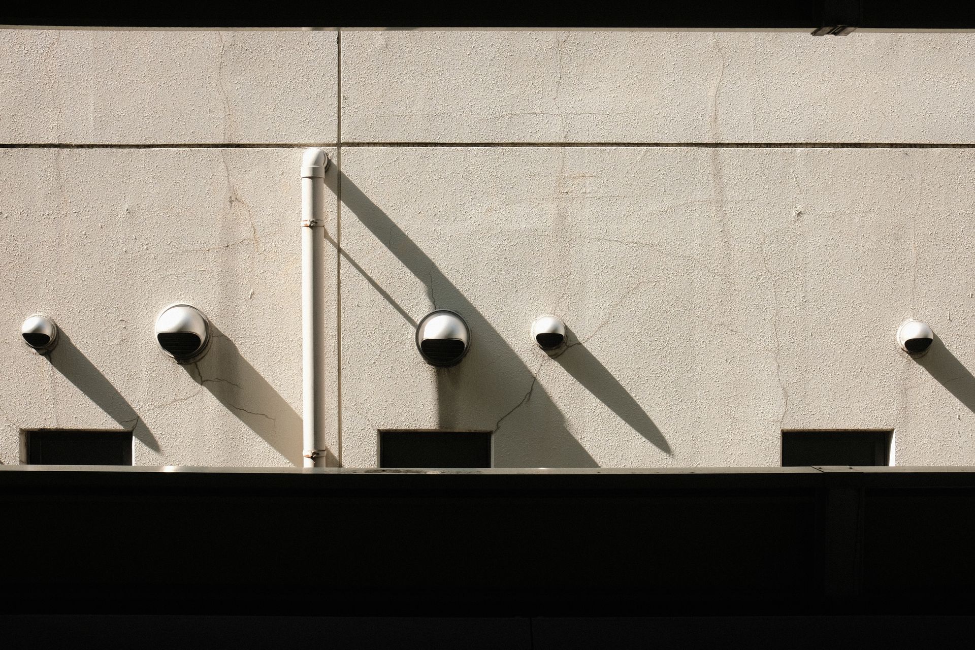 A minimalist wall featuring multiple security cameras casting long shadows in the sunlight.
